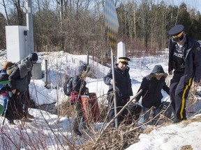 RCMP officers help a family of asylum claimants as they cross the border into Canada from the United States, Monday, February 20, 2017 near Hemmingford, Que.