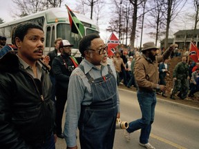 FILE -In this Jan. 18, 1987, photo, Atlanta city councilman, Rev. Hosea Williams, in overalls, leads a march against efforts to keep Forsyth County in Georgia all white past counter-protesters near Cumming, Ga., as a crowd waves Confederate flags and jeer the marchers. Racial stereotypes and racist imagery in popular culture seemed to be everywhere in the chaotic 1980s when future Virginia Gov. Ralph Northam and future Attorney General Mark Herring admitted dressing up in blackface.