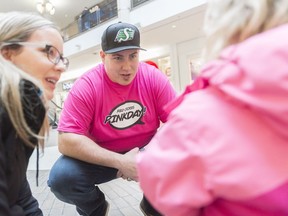 Saskatchewan Roughriders center Dan Clark, center, speaks to the daughter of Christa Hovind, right, after giving them a Pink Day T-shirt. The Red Cross, with Clark's help, gave away the shirts to raise awareness about bullying.