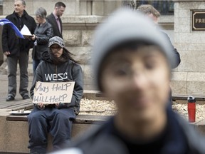 A man holds a sign up behind Saima Desai who organized the Fight for $15 Saskatchewan "DEAD LAST" event, a street party/protest to 'celebrate' the fact that Saskatchewan has the worst minimum wage in the country. The event was held over the noon hour on Scarth Street and 11th Avenue.