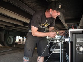 Riley Richter of Capitol Staging works to install electrical cords beneath the stage for Regina Folk Festival in Victoria Park.