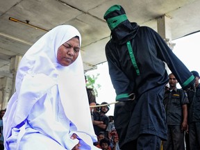 A crowd watch an unidentified "punk" Indonesian female (L), who was caught having pre-marital sex in public with a male partner, being caned by a sharia police officer dressed in black robes at a public square in Langsa town on April 20, 2012. AFP PHOTO / RIZA LAZUARDI