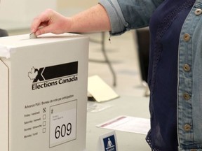 A voter drops her ballot in the box while taking part in an advance poll for the federal election on October 9, 2015.