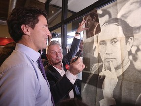 Liberal leader Justin Trudeau looks at a poster of his late father, former Prime Minister Pierre Trudeau, during a campaign stop at a coffee shop in Sainte-Therese, Quebec, October 15, 2015.