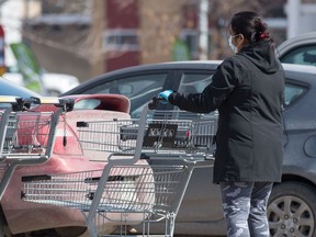 A person wearing rubber gloves and a surgical mask during the COVID-19 pandemic returns a shopping cart at a grocery store in Regina, Saskatchewan on March 26, 2020.