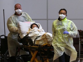 Paramedics dressed in protective clothing guide a stretcher carrying an ill woman from a Westjet flight from Vancouver to a waiting ambulance at Richardson International Airport in Winnipeg, Manitoba, Feb. 27, 2020.