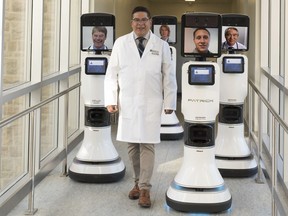 Dr. Ivar Mendez walks alongside remote controlled robots used to allow doctors to interact with patients in far-flung locations.