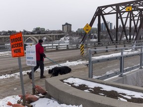 A man walks his dog past signs informing pedestrians which side of the Traffic Bridge to travel in Saskatoon, SK on Wednesday, April 1, 2020.