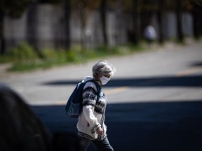 A woman wearing a fabric mask on her face walks in downtown Vancouver, on Thursday, April 16, 2020. Infectious disease experts say provinces looking to relax restrictions related to COVID-19 need to consider their neighbours in those decisions.