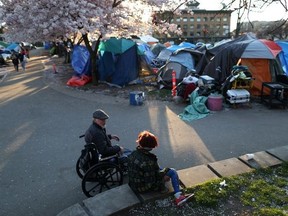 People sit near a homeless encampment at Oppenheimer Park as the local health unit has started prescribing a "safe supply" of narcotic alternatives to combat overdoses due to poisonous additives and to support addicts and the homeless into practicing social distancing to help slow the spread of coronavirus disease (COVID-19) in the Downtown Eastside of Vancouver, April 7, 2020.