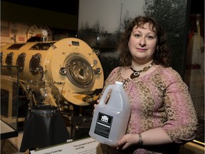 Julia Petrov, Royal Alberta Museum curator of daily life and leisure, holds a bottle of locally produced hand sanitizer, an artifact from the COVID-19 pandemic. Beside her is an iron lung from the museum's display depicting the 1950s polio epidemic.