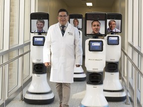 Dr. Ivar Mendez walks alongside remote controlled robots used to allow doctors to interact with patients in far-flung locations.