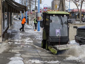 Workers clear snow on the sidewalk of Second Avenue South on March 24, 2020.