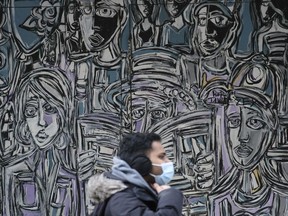 A masked pedestrian walks past a mural in downtown Regina on March 24, 2021. A day earlier, the provincial government announced new restrictions in an effort to limit rising COVID-19 numbers in the city.