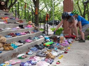 A mother and son place a letter among 215 shoes on the steps of St. Paul's Cathedral in Saskatoon, in honour of the 215 children from a B.C. residential school whose bodies were found last week. Photo taken on May 31, 2021. (Saskatoon StarPhoenix / Michelle Berg)