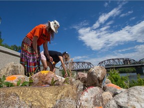 Elder Marjorie Beaucage, left, paints a stone orange near River Landing. Youth-led Chokecherry Studios invited the community to paint 215 stones along the Saskatchewan River to honour the 215 Indigenous children found in an unmarked grave at a former Kamloops Residential School in BC. Photo taken in Saskatoon, SK on Friday, June 4, 2021.