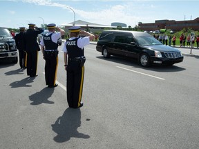 RCMP members salute while watching a procession of police vehicles following a hearse down Dewdney Avenue in Regina, Saskatchewan on June 15, 2021. The procession passed by RCMP 'F' Division headquarters Tuesday following the June 12 on-duty death of RCMP Const. Shelby Patton in Wolseley, Saskatchewan.