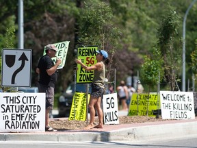 Two people converse while holding signs promoting conspiracy theories on Victoria Avenue in Regina, Saskatchewan on July 24, 2021.