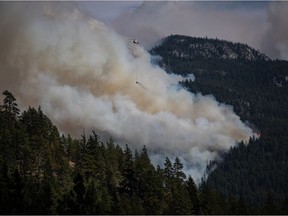 CP-Web. A helicopter carrying a water bucket flies past the Lytton Creek wildfire burning in the mountains near Lytton, B.C., on Sunday, August 15, 2021.
