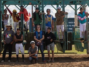 Tim Moccasin crouches down for a group photo with the other jockeys who competed in the last flat race at Marquis Downs, in front of the historic starting gate. Photo taken in Saskatoon on Aug. 29.