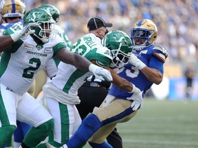 Winnipeg Blue Bombers running back Andrew Harris (right) throws Saskatchewan Roughriders defensive back Christian Campbell to the ground by the helmet as defensive tackle Micah Johnson tries to get at Harris during a fracas in Saturday's Banjo Bowl.