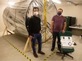 Anwit Adhikari, left, and Samuel Reddekop stand in front of the mock up of an airlock at Innovation Place in Regina, Saskatchewan on Oct. 15, 2021. The airlock is designed to accommodate astronauts on Mars. The two men worked together on the project, along with a number of other people, not pictured.
