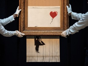 LONDON, ENGLAND - OCTOBER 12: Sotheby's employees pose with 'Love is in the Bin' by British artist Banksy during a media preview at Sotheby's auction house on October 12, 2018 in London, United Kingdom. During Sotheby's Contemporary Art Sale on 5th October the Banksy artwork 'Girl with Balloon' shredded through the bottom of the frame as it was sold. With Banksy being responsible for the shredding, the buyer has agreed to proceed with the sale and it is now titled 'Love is in the Bin' and said to be worth more than the £1.04million paid