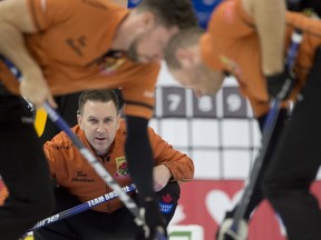 Saskatoon SK,November 28, 2021.Tim Hortons Curling Trials.Skip Brad Gushue sits in the rings as (L-R) 2nd.Brett Gallant and lead Geoff Walker bring the stone into the house during mens final agains team Jacobs.Curling Canada/ Michael Burns Photo