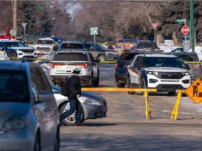 A pedestrian looks on as police vehicles remain at the intersection of 22nd Street West and Avenue U South in Saskatoon, Sask. on Feb. 23, 2022.