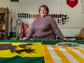 The Flag Shop owner and manager Judy Denham stands for a photo with Saskatoon (right) and Moose Jaw (left) municipal flags laid out on a table at her business in Saskatoon.