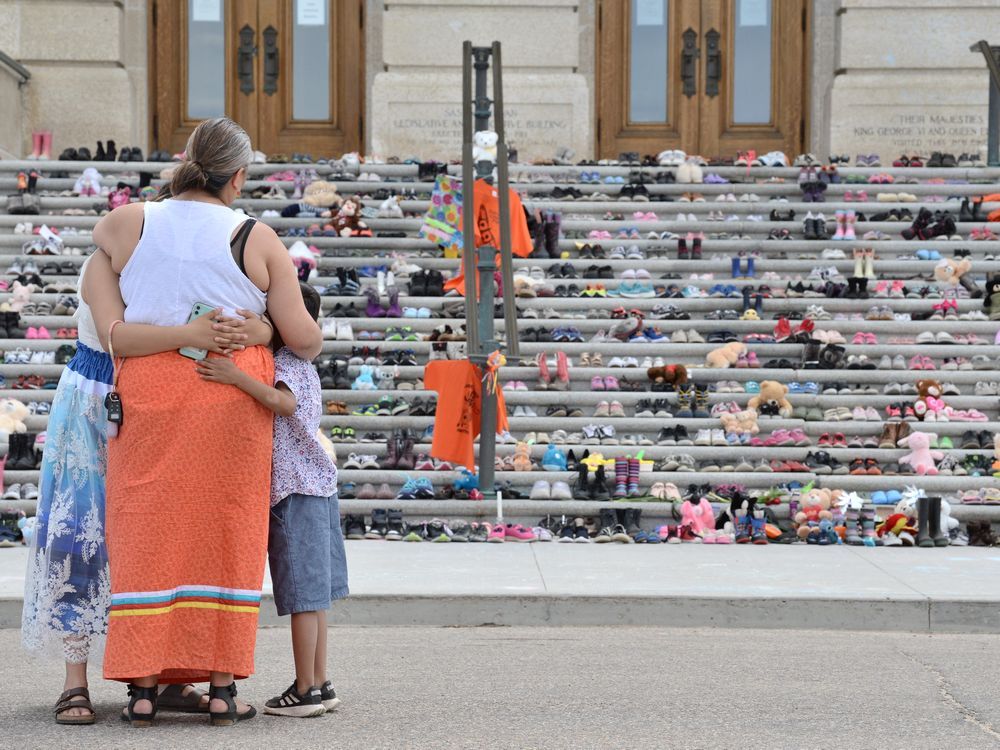 People embrace while observing a display of children's shoes representing children who died while in Canada's residential school program on the steps of the Saskatchewan Legislative Building in Regina, Saskatchewan on May 31, 2021.