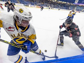 Saskatoon Blades forward Kyle Crnkovic (16) and Moose Jaw Warriors defenceman Lucas Brenton (3) battle for the puck in the corner during first-period WHL playoff action in Saskatoon on Tuesday, April 26, 2022.