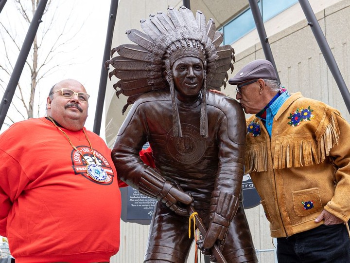  Neil Sasakamoose (left) with the statue of his father Fred Sasakamoose during its unveiling at SaskTel Centre. Eugene Arcand from Muskeg Lake Cree Nation gave a kiss to the statue. Photo taken in Saskatoon on May 18, 2022.