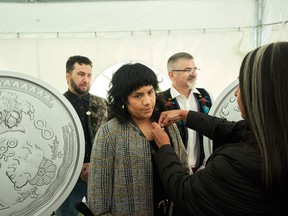 Executive Director of the National Centre for Truth and Reconciliation Stephanie Scott, right, places a pin on artist Leticia Spence, as fellow artists Jason Sikoak, left, and JD Hawk watch as they attend the unveiling of the 2022 Truth and Reconciliation Keepsake at the National Centre for Truth and Reconciliation in Winnipeg, Thursday, Sept. 22, 2022. The artists collaborated on the creation of the Keepsake.