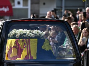 Members of the public pay their respects as they hearse carrying the coffin of Queen Elizabeth II, draped in the Royal Standard of Scotland, is driven through Ballater, on September 11, 2022.