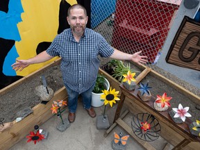 Will Livingston stands for a photo surrounded by some of his metal flower creations outside of his workshop at Saskatoon Makerspace.