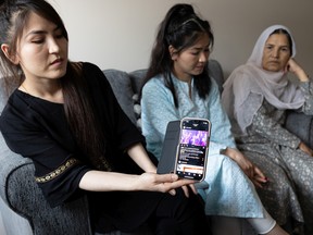 Shakiba Ahmadi (left) holds up a video of her older sister singing while Rejna and their mom Zubida Yousfi listen. The family is split up around the world, as they fled the Taliban and went to whichever country would accept them. Photo taken in Saskatoon on May 17, 2022.