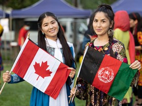 Rejna Ahmadi (left) and her sister Shakiba Ahmadi hold up the Canadian and Afghanistan flags at the Fringe festival on Broadway Avenue in Saskatoon on Aug. 3, 2022.