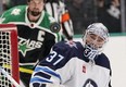 The puck deflects off of Winnipeg Jets goaltender Connor Hellebuyck as Dallas Stars left winger Jamie Benn looks on Friday night in Dallas. The Stars would later score a contentious goal on Hellebuyck after Benn bulldozed him and ripped the goalie mask clear off the netminder’s head. The Jets went on to win 5-4 in overtime.