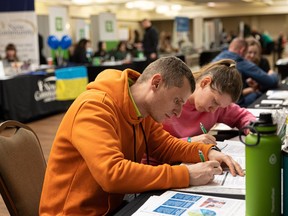 Volodymyr Darda, 34, and Hanna Darda, 29, from Kryvyi Rih, Ukraine, fill out forms at the Sask Jobs booth at the Travelodge hotel event in Saskatoon on Friday.