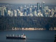 A bulk carrier cargo ship travels into port as a Harbour Air seaplane flies towards Stanley Park and the downtown skyline, in Vancouver, on Wednesday, July 27, 2022.