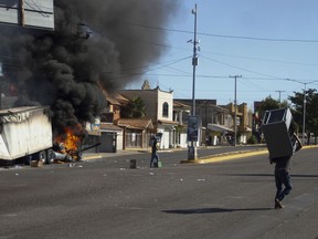 Men carry furniture after looting a store, as a truck burns on a street in Culiacan, Sinaloa state, Thursday, Jan. 5, 2023.