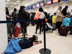 A passenger sleeps as other passengers from Sunwing airlines line up for check-in at Cancun International Airport after many flights to Canada have been canceled because of the severe winter weather conditions in various parts of the country, in Cancun, Mexico December 27, 2022. REUTERS/Paola Chiomante