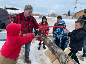 Peter Durocher (second from left) teaches Kayton Daigneault (left) and Darius Moate (right) how to saw through a log with a hand saw at the Métis cultural festival in île-à-la-Crosse, Sask. on March 31, 2023. (Julia Peterson/Saskatoon StarPhoenix)