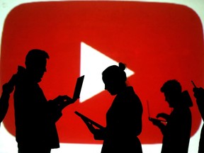 Silhouettes of laptop and mobile device users are seen next to a screen projection of the YouTube logo in this picture illustration.