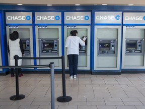 In this March 24, 2020 file photo, a Chase bank employee, right, cleans the branches ATMs as a customer uses another in the Flushing neighborhood of the Queens borough of New York.
