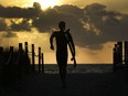 A surfer heads to the beach to catch some waves as the sun rises over the Atlantic Ocean, in Surfside, Fla., Thursday, April 6, 2023. Experts say it's important to take stock of your overall finances before deciding how to spend a tax refund.