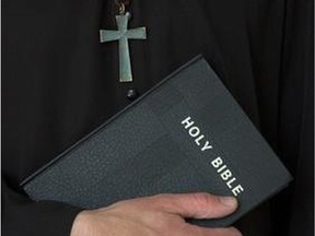 A priest wearing a crucifix holds a Bible.