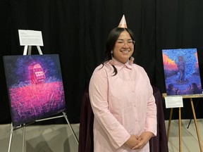 Azby Whitecalf stands with two of their paintings at a masquerade ball fundraiser for LGBTQ2S+ education in Battlefords Agency Tribal Chiefs (BATC) communities.