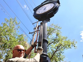 Jeff Golding, building production manager at The StarPhoenix, hoists a roughly 8 kg (17.8 pound)antique thermostat up the pillar of the clock that stands on the grounds of the former newspaper building.